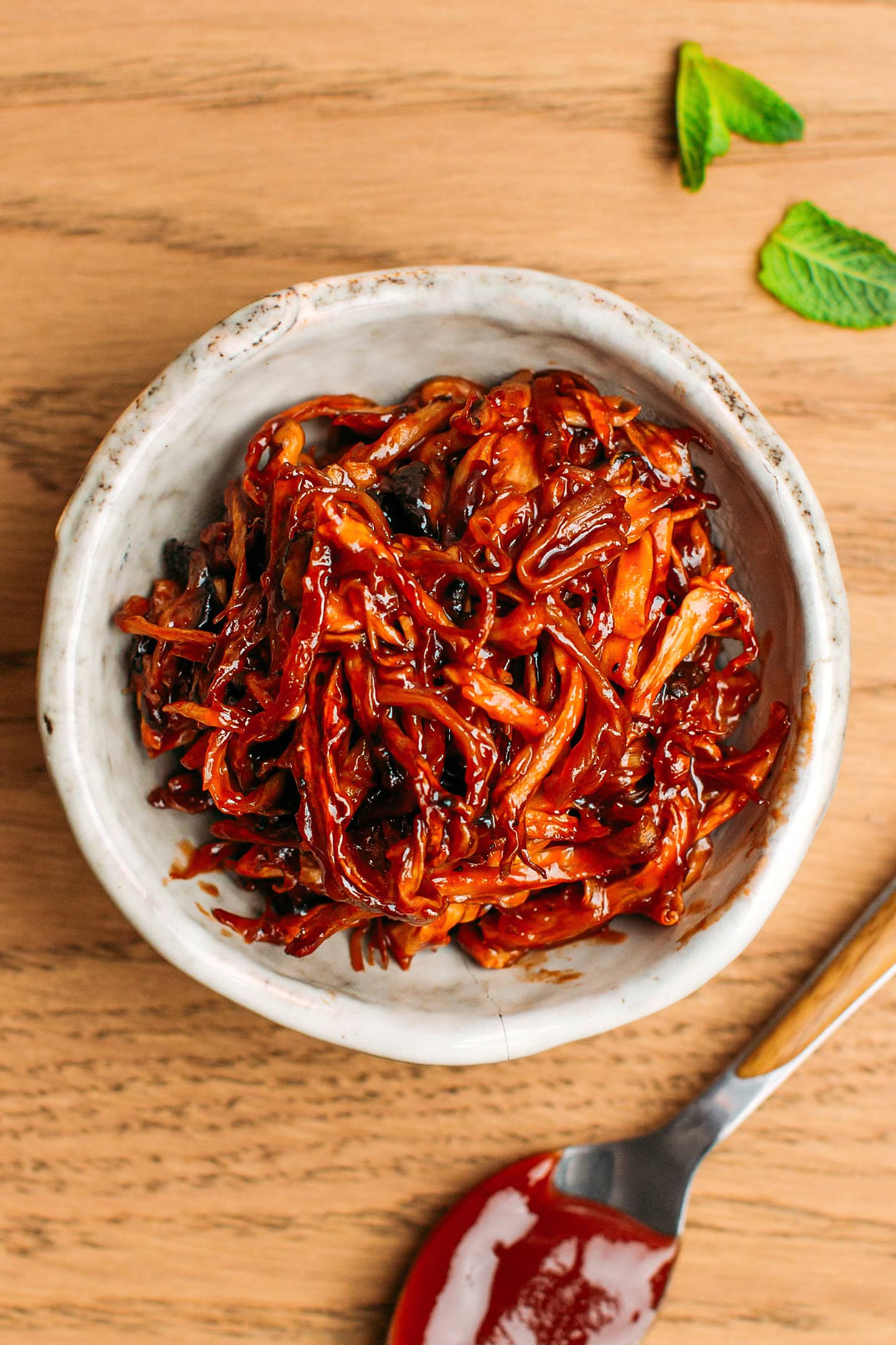 Small bowl containing pulled mushrooms coated with barbecue sauce.