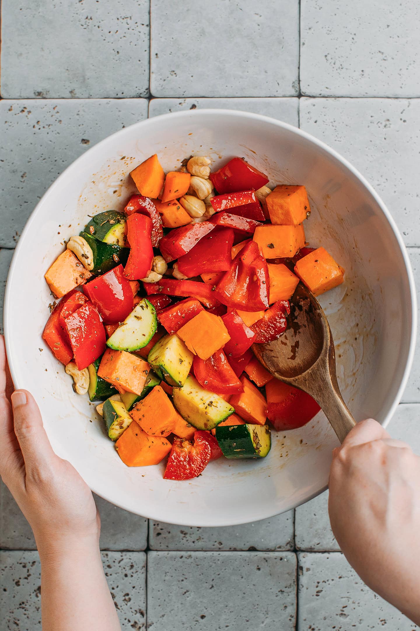 Tossing diced sweet potato, bell pepper, and zucchini with oil.